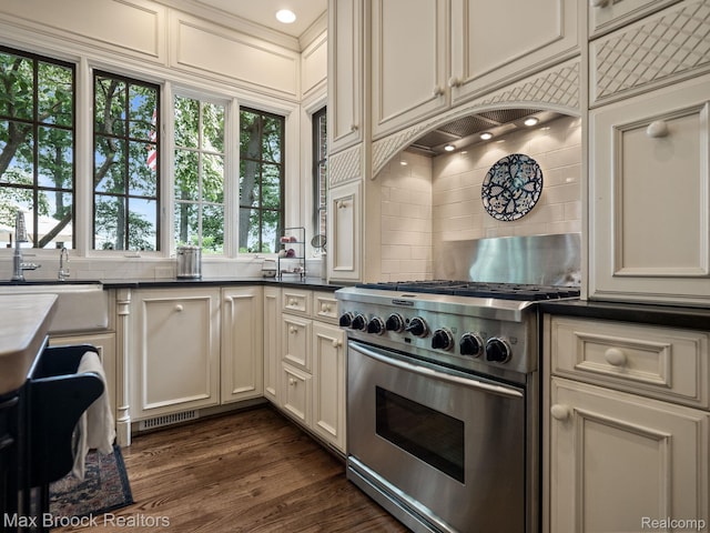 kitchen with stainless steel stove, backsplash, dark countertops, and dark wood-style floors
