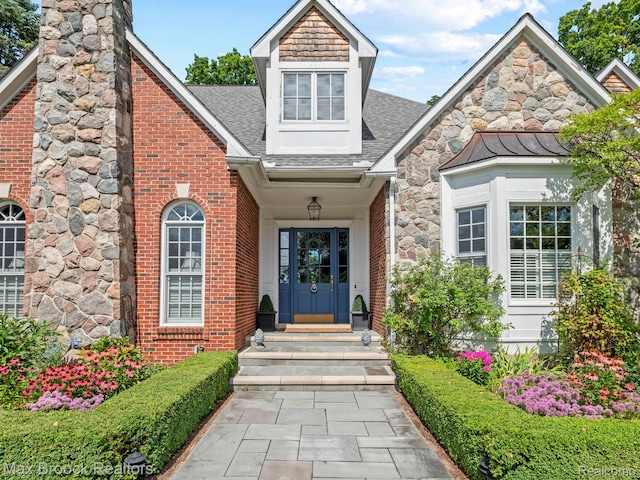 entrance to property with a shingled roof, brick siding, and a chimney