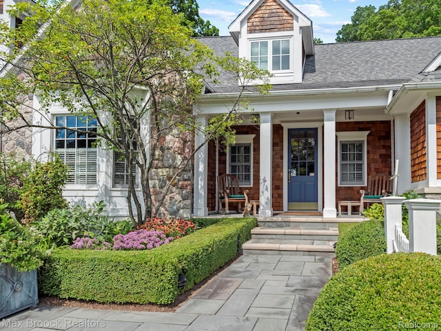 view of exterior entry featuring roof with shingles and covered porch