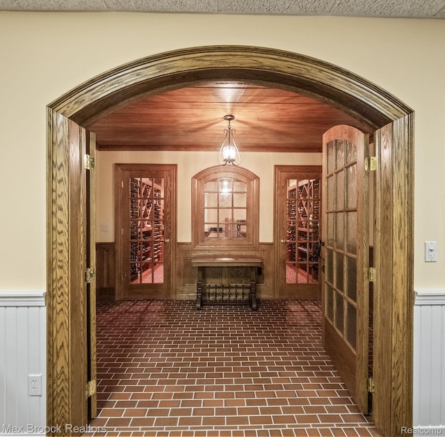 wine cellar with arched walkways, wainscoting, and brick patterned floors