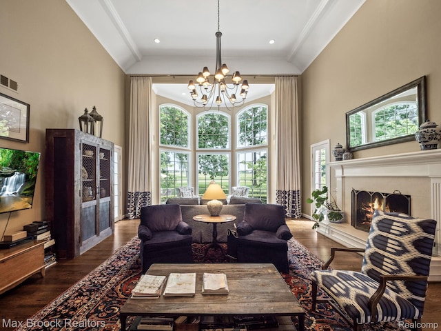 living area featuring a chandelier, a high ceiling, a lit fireplace, ornamental molding, and wood finished floors