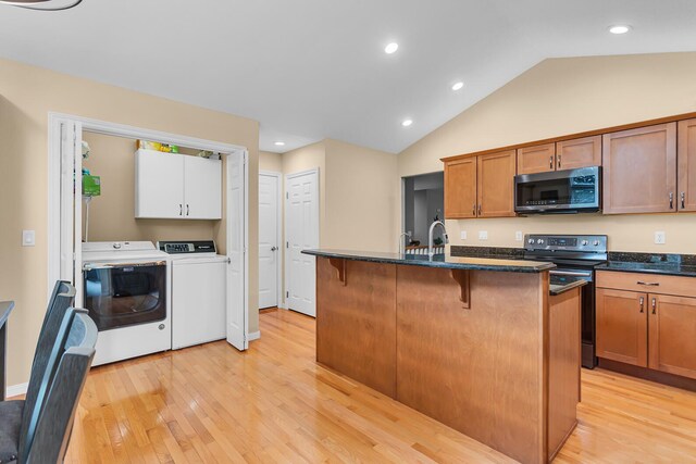 4268 Fairway Ln, Jackson, MI 49201 - kitchen featuring black electric range, washing machine and clothes dryer, light wood-type flooring, a kitchen breakfast bar, and vaulted ceiling