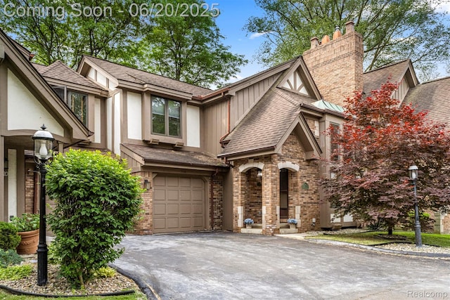 718 S Military St, Dearborn, MI 48124 - tudor-style house with driveway, an attached garage, board and batten siding, a shingled roof, and a chimney