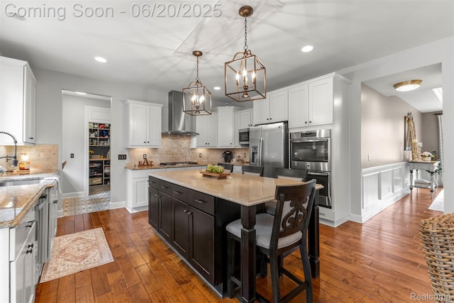 23736 Point O Woods Ct, South Lyon, MI 48178 - kitchen featuring appliances with stainless steel finishes, wall chimney exhaust hood, a chandelier, white cabinets, and a center island