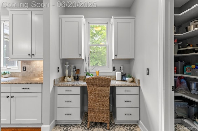 23736 Point O Woods Ct, South Lyon, MI 48178 - kitchen featuring built in study area, white cabinetry, backsplash, light stone countertops, and tile patterned floors