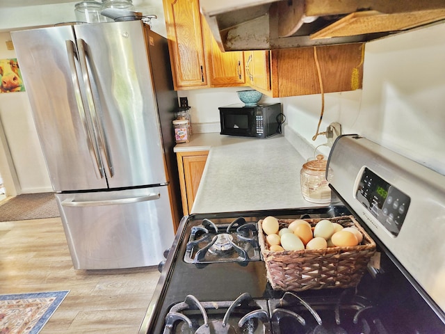 350 S Catalpa Ave, White Cloud, MI 49349 - kitchen with appliances with stainless steel finishes, under cabinet range hood, light wood-type flooring, light countertops, and brown cabinetry