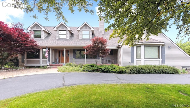 459 N Elms Rd, Flushing, MI 48433 - new england style home with a chimney, a front yard, covered porch, and a shingled roof