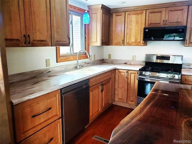 115 Choctaw Trl, Prudenville, MI 48651 - kitchen featuring appliances with stainless steel finishes, dark wood-style floors, pendant lighting, and brown cabinetry