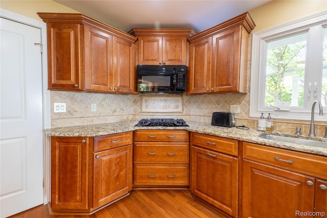19891 Parke Ln, Grosse Ile, MI 48138 - kitchen with black appliances, wood finished floors, light stone countertops, decorative backsplash, and brown cabinetry
