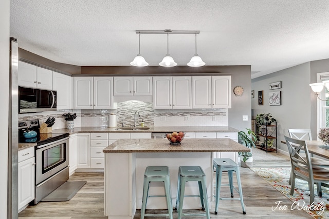 278 Caravan Rd, Norton Shores, MI 49441 - kitchen featuring appliances with stainless steel finishes, light wood-style floors, a textured ceiling, a breakfast bar, and tasteful backsplash