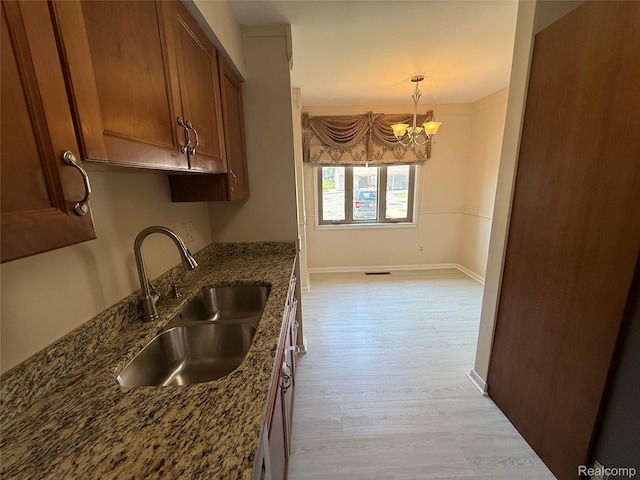 6352 Laurentian Ct, Flint, MI 48532 - kitchen featuring a chandelier, brown cabinetry, light wood-type flooring, dark stone countertops, and hanging light fixtures