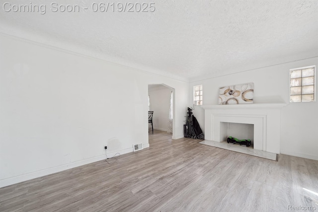 15477 Lauder St, Detroit, MI 48227 - unfurnished living room featuring a textured ceiling, healthy amount of natural light, wood finished floors, arched walkways, and a fireplace with flush hearth