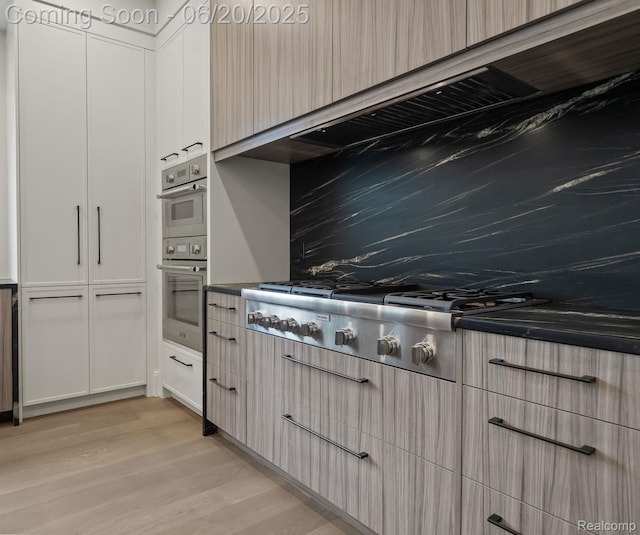 1120 Lyonhurst St, Birmingham, MI 48009 - kitchen featuring appliances with stainless steel finishes, light wood-style flooring, exhaust hood, and dark countertops