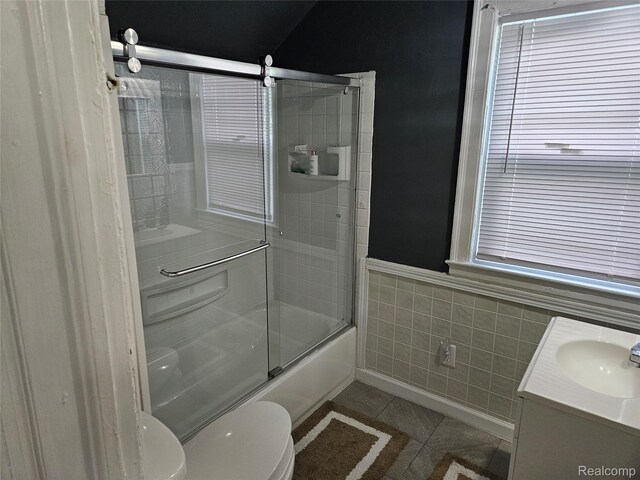 4294 W Buena Vista St, Detroit, MI 48238 - full bathroom with tile patterned flooring, tile walls, shower / bath combination with glass door, vanity, and a wainscoted wall