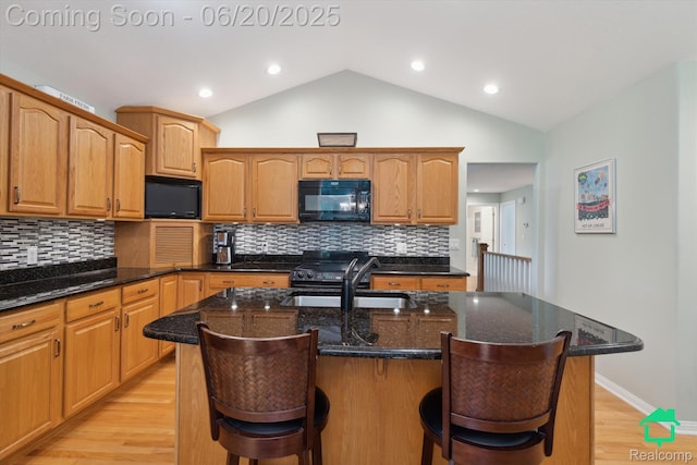 4273 Fairway Ln, Jackson, MI 49201 - kitchen with black microwave, light wood-style flooring, a breakfast bar area, dark stone counters, and vaulted ceiling