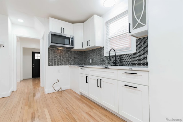 15821 Kentfield St, Detroit, MI 48223 - kitchen with stainless steel microwave, decorative backsplash, light countertops, white cabinetry, and light wood-style floors