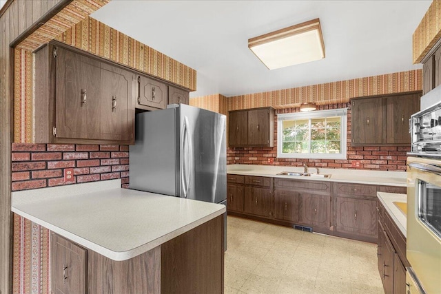 360 Wood Creek Dr, Howell, MI 48843 - kitchen with wallpapered walls, light floors, light countertops, freestanding refrigerator, and a peninsula