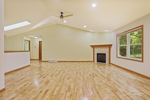878 S Crooked Tree Ln, Midland, MI 48640 - unfurnished living room featuring light wood-style floors, a ceiling fan, a tile fireplace, lofted ceiling, and a skylight