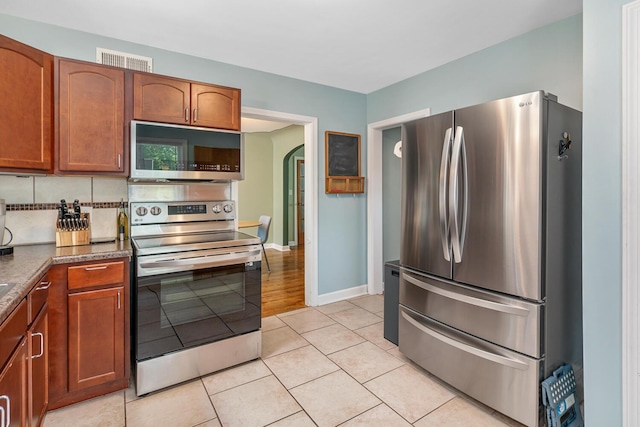 2646 Forest Grove Ave SW, Wyoming, MI 49519 - kitchen featuring stainless steel appliances, light tile patterned flooring, arched walkways, and brown cabinetry