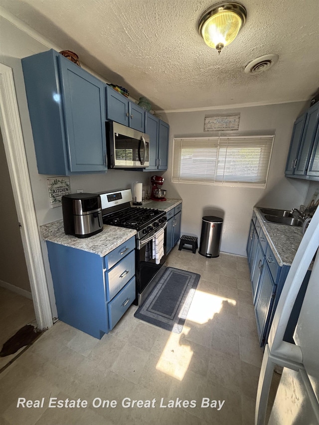 1521 Stanley St, Saginaw, MI 48602 - kitchen featuring appliances with stainless steel finishes, blue cabinetry, a textured ceiling, light flooring, and light countertops