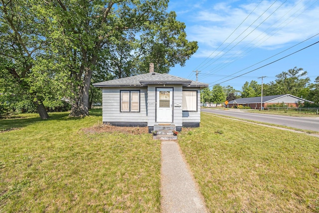 2201 Riordan St, Muskegon Heights, MI 49444 - view of front facade featuring entry steps, a chimney, a front lawn, and roof with shingles