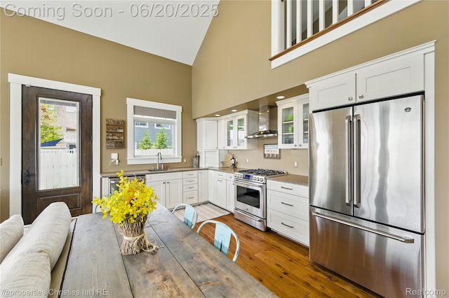 11693 Kenton Dr, Whitmore Lake, MI 48189 - kitchen with high quality appliances, wall chimney range hood, high vaulted ceiling, white cabinets, and wood-type flooring