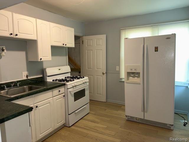 19670 Mccormick St, Detroit, MI 48224 - kitchen with white appliances, white cabinets, light wood-style floors, and dark countertops