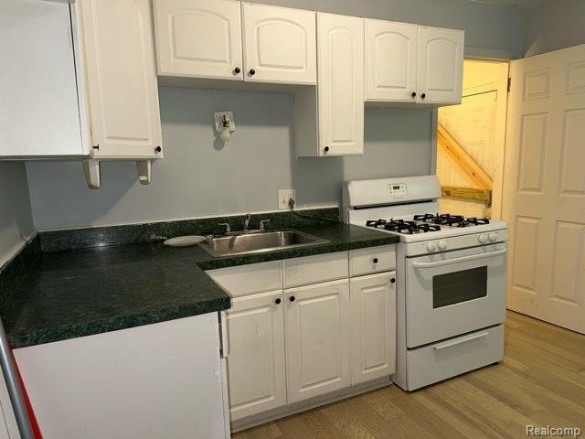 19670 Mccormick St, Detroit, MI 48224 - kitchen featuring white gas stove, white cabinets, dark countertops, and light wood-style flooring