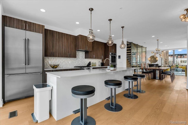 248 Alfred St, Detroit, MI 48201 - kitchen with stainless steel appliances, light wood-style flooring, decorative backsplash, a kitchen bar, and dark brown cabinetry