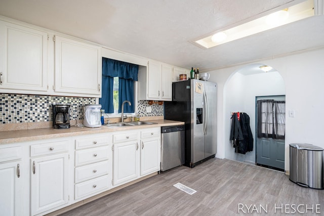 10340 Kartz Rd, Greenville, MI 48838 - kitchen with appliances with stainless steel finishes, arched walkways, backsplash, white cabinets, and light wood-type flooring