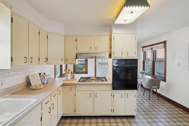 34 Charles St, Hillsdale, MI 49242 - kitchen featuring black oven, cream cabinetry, stainless steel gas cooktop, under cabinet range hood, and backsplash