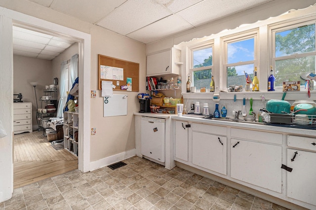 724 E Ludington Ave, Ludington, MI 49431 - kitchen featuring a paneled ceiling, white dishwasher, white cabinets, light countertops, and healthy amount of natural light