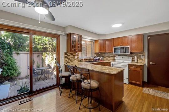 7190 Pebble Park Dr, West Bloomfield, MI 48322 - kitchen with white electric stove, stainless steel microwave, a breakfast bar, brown cabinetry, and a peninsula