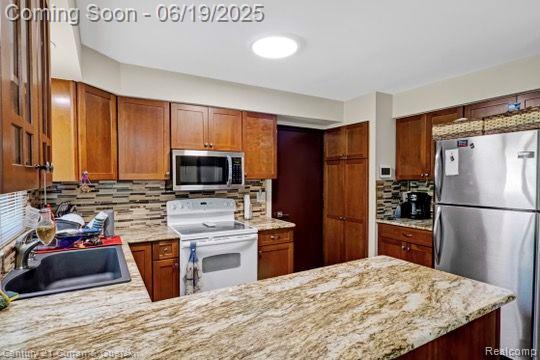 7190 Pebble Park Dr, West Bloomfield, MI 48322 - kitchen with appliances with stainless steel finishes, tasteful backsplash, brown cabinetry, and light stone counters