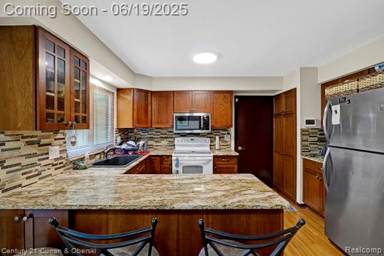 7190 Pebble Park Dr, West Bloomfield, MI 48322 - kitchen with appliances with stainless steel finishes, a peninsula, glass insert cabinets, light wood-style flooring, and backsplash