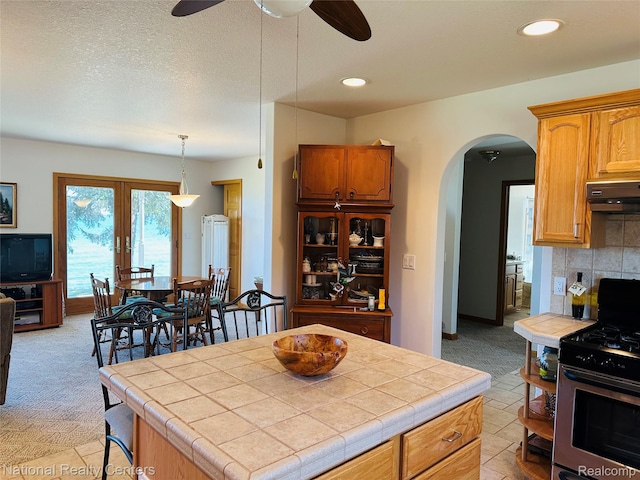 1390 N US-23, East Tawas, MI 48730 - kitchen with stainless steel gas range oven, tile countertops, range hood, arched walkways, and light colored carpet