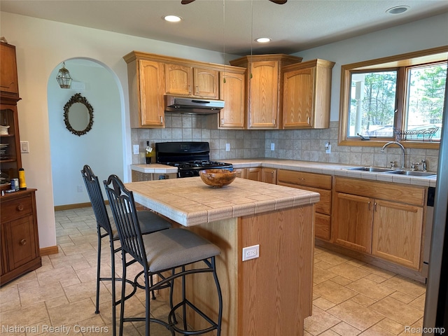 1390 N US-23, East Tawas, MI 48730 - kitchen featuring under cabinet range hood, black range, tile countertops, a kitchen bar, and tasteful backsplash