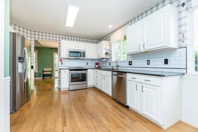 3105 Earlmoore Ln, Ann Arbor, MI 48105 - kitchen with appliances with stainless steel finishes, light wood-type flooring, dark countertops, white cabinetry, and backsplash