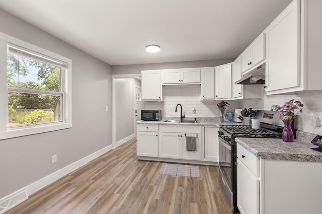 645 Amity Ave, Muskegon, MI 49442 - kitchen featuring stainless steel gas stove, under cabinet range hood, black microwave, tasteful backsplash, and light countertops