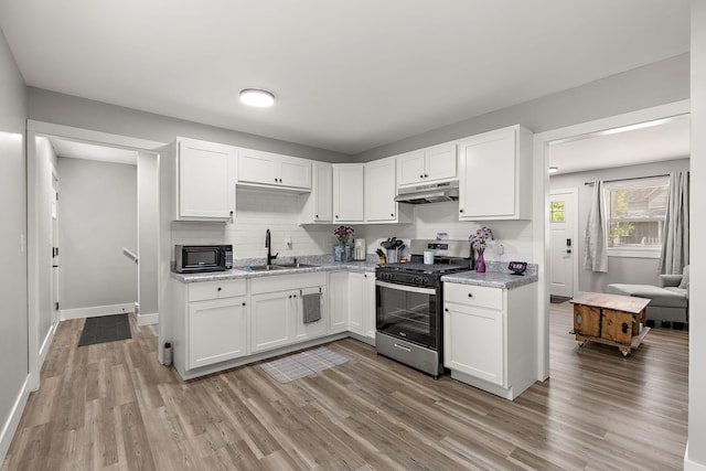 645 Amity Ave, Muskegon, MI 49442 - kitchen with stainless steel gas range, under cabinet range hood, black microwave, white cabinets, and light wood finished floors