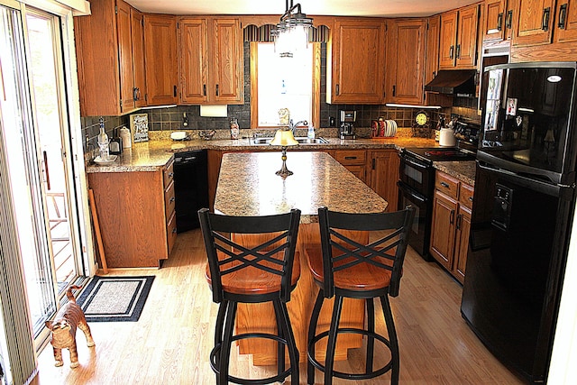 7680 S Warner Ave, Fremont, MI 49412 - kitchen with black appliances, light wood-style floors, under cabinet range hood, and a center island
