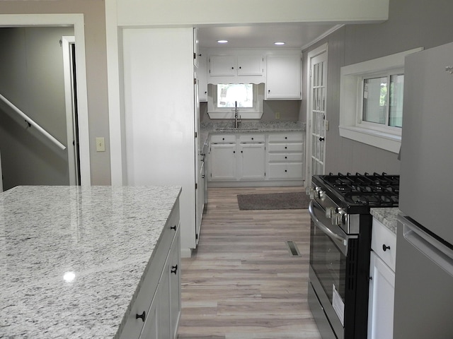 26370 S Shore Dr, Mendon, MI 49072 - kitchen with freestanding refrigerator, stainless steel gas stove, light wood-type flooring, white cabinetry, and light stone counters