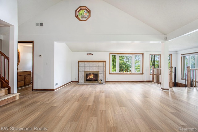 332 Community Dr, Battle Creek, MI 49014 - unfurnished living room with high vaulted ceiling, light wood-style flooring, stairs, and a tiled fireplace