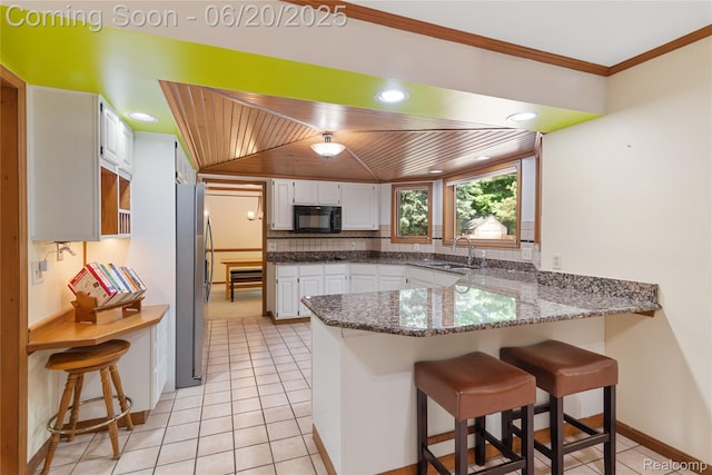1484 Kings Pointe Rd, Grand Blanc, MI 48439 - kitchen featuring black microwave, a peninsula, freestanding refrigerator, wooden ceiling, and white cabinetry