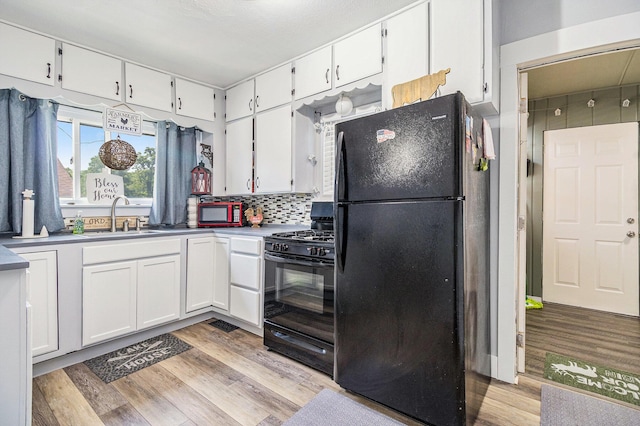 378 Goguac St W, Battle Creek, MI 49015 - kitchen with black appliances, white cabinets, light wood-style flooring, and backsplash