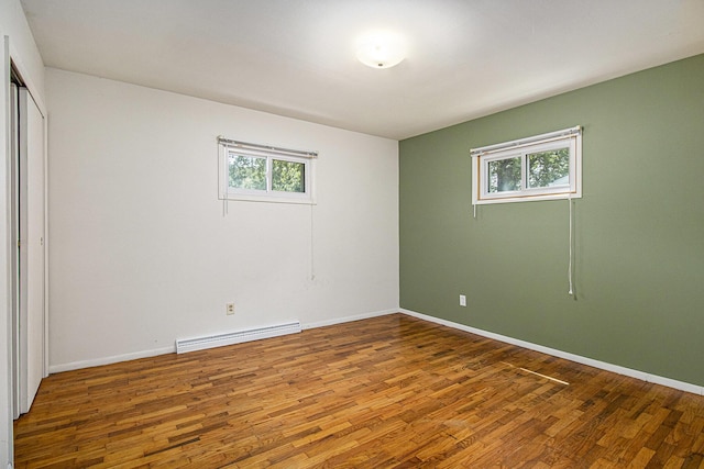 8814 S Sprinkle Rd, Portage, MI 49002 - unfurnished bedroom featuring baseboard heating, wood finished floors, multiple windows, and a closet
