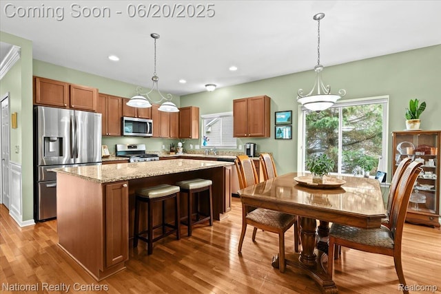 332 Asbury Ct, Highland, MI 48357 - kitchen with stainless steel appliances, a center island, brown cabinetry, light wood finished floors, and pendant lighting
