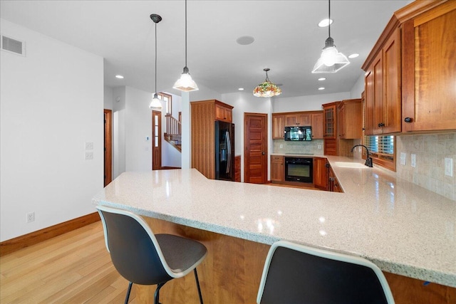 4679-4681 Forest Ridge Dr, Holland, MI 49423 - kitchen with black appliances, brown cabinets, decorative backsplash, a peninsula, and light stone countertops