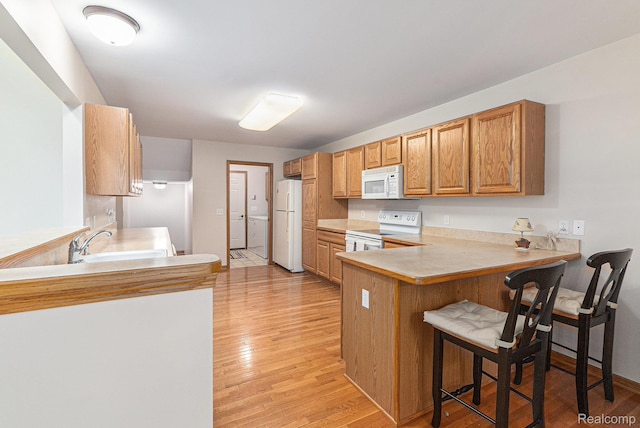 6144 Northridge Hills Dr, Brighton, MI 48116 - kitchen with white appliances, light wood-style floors, a peninsula, and a kitchen breakfast bar