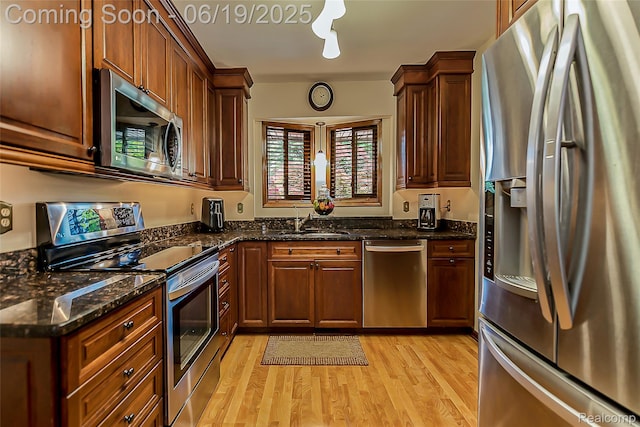 24320 Simmons Dr, Novi, MI 48374 - kitchen featuring stainless steel appliances, light wood-type flooring, dark stone counters, and brown cabinetry